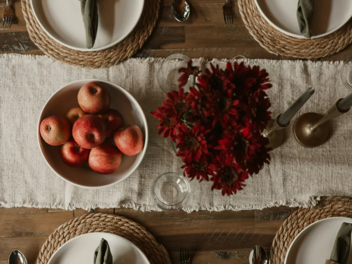 Table seen from above with a linen runner, a bowl of red apples and dark red flowers