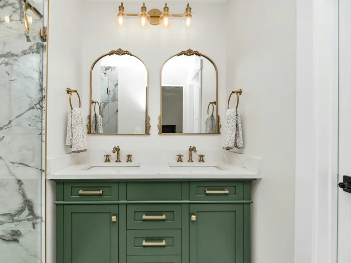 Bathroom with a green double vanity, two arched brass mirrors and a marble shower wall
