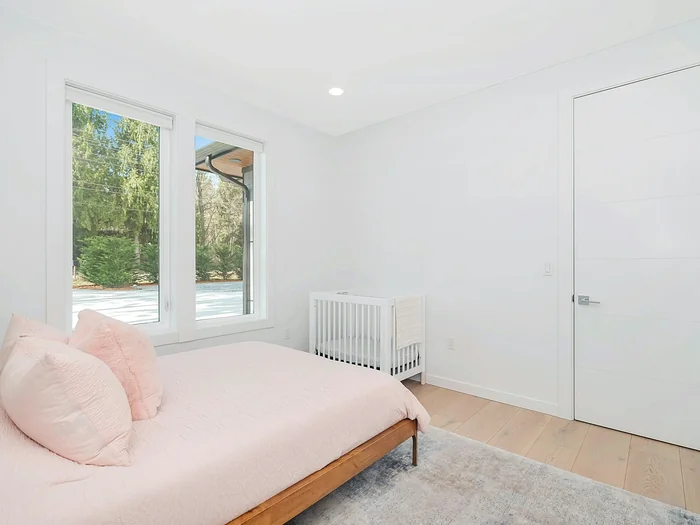 Bright bedroom with a low wooden bed, pale walls, a fitted wardrobe and a window onto trees
