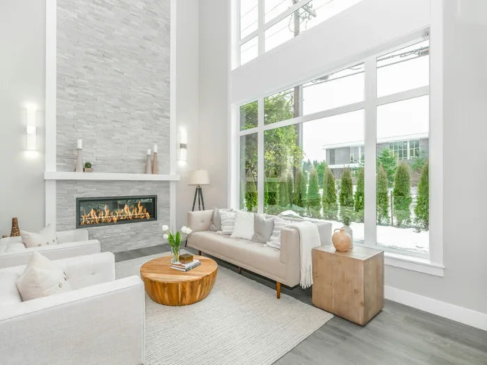 Double-height living room with floor-to-ceiling windows onto the garden, a stone-clad fireplace and cream sofas