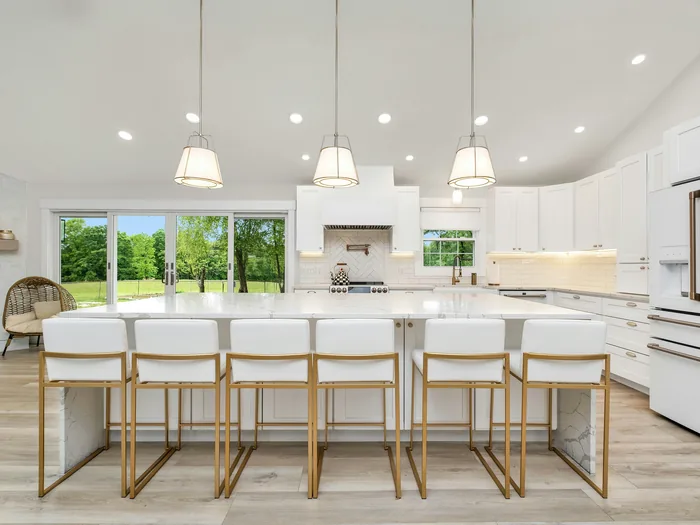 Finished kitchen with a long marble island, six bar stools and white shaker units