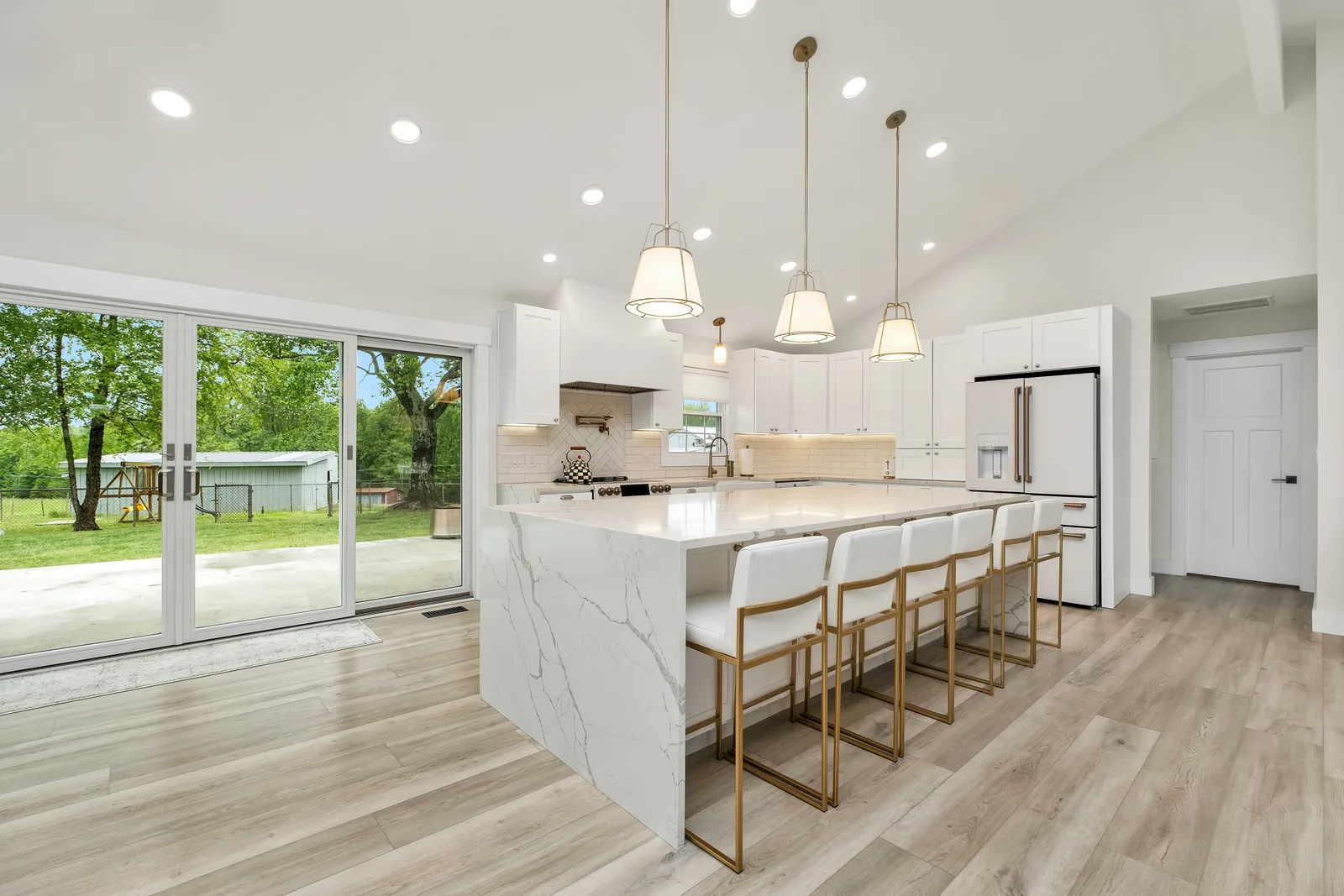 Finished open-plan kitchen with a marble island, six bar stools and sliding doors onto the garden