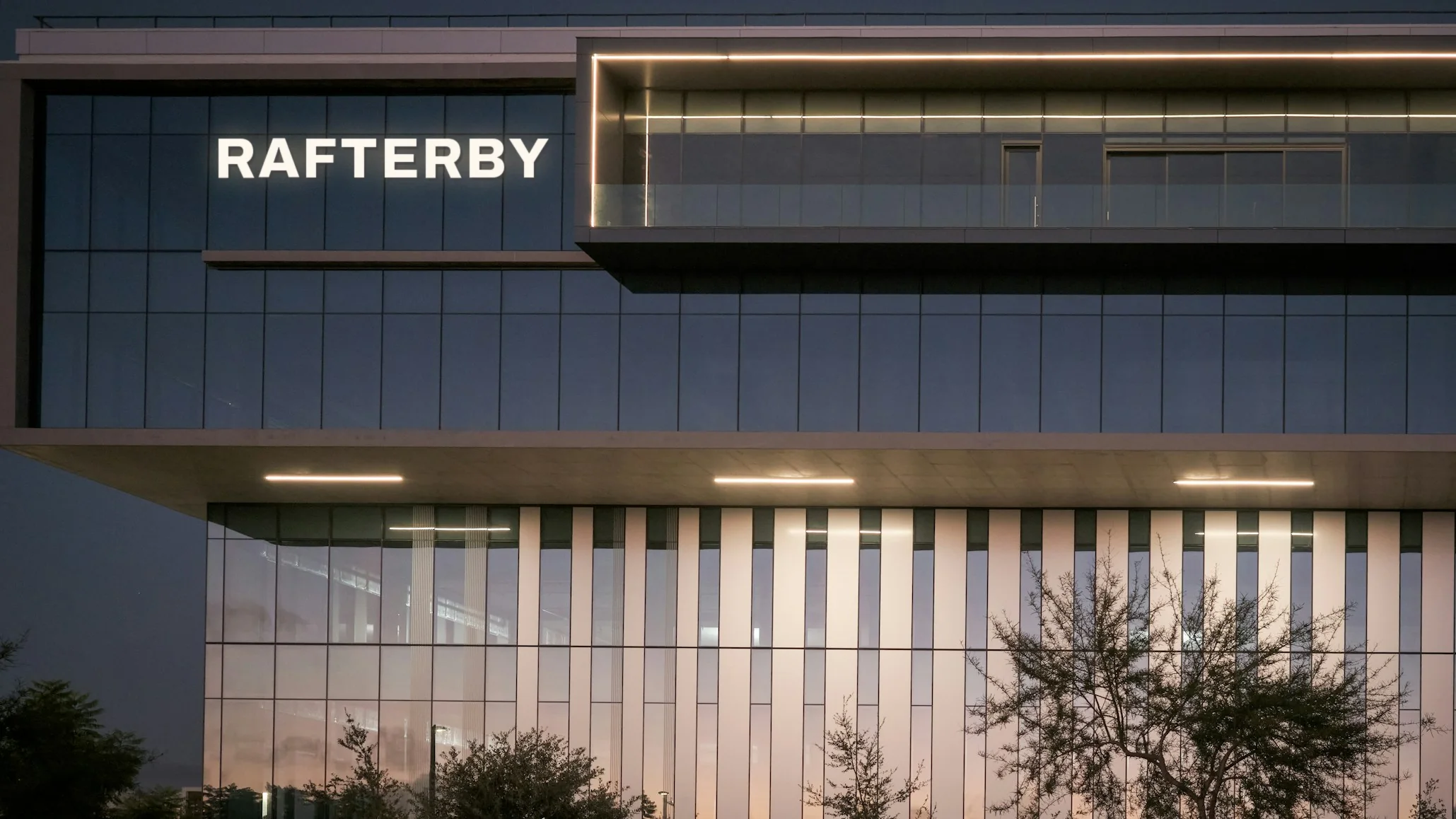 Modern glass headquarters with RAFTERBY lettering on the facade at dusk