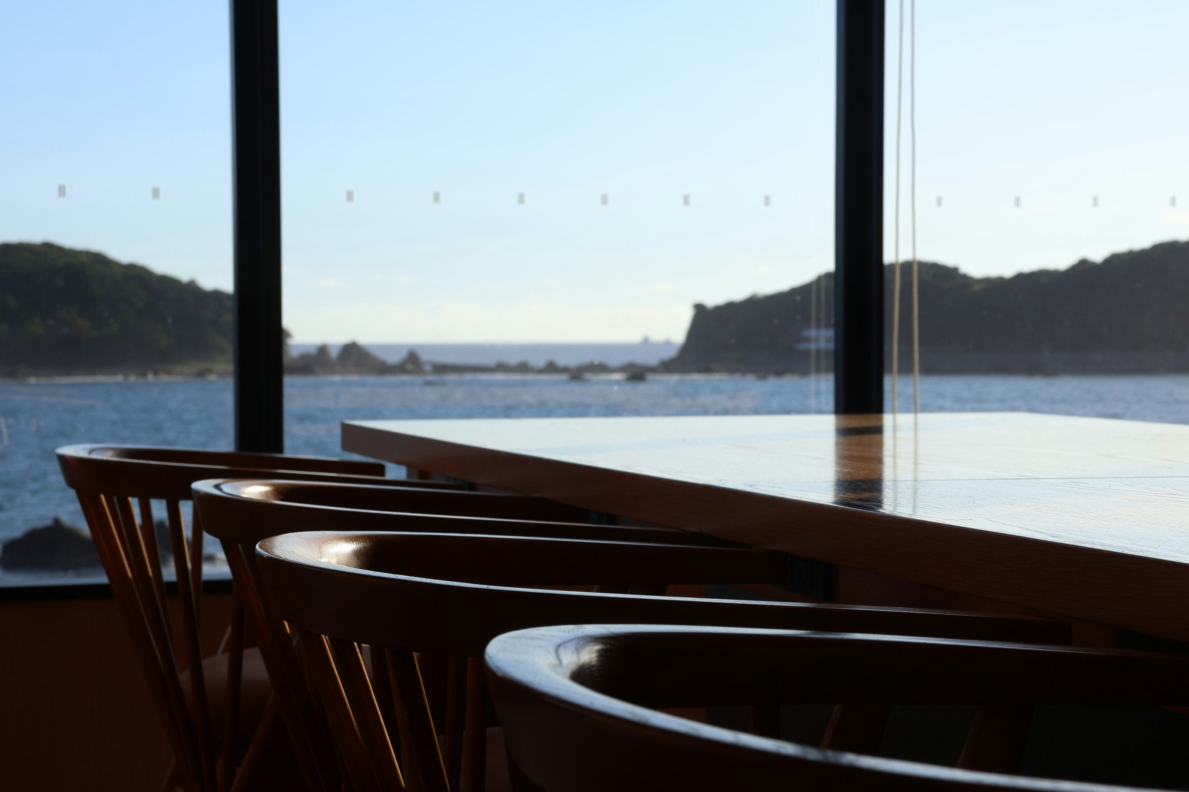 A hotel bar counter and timber seating beside broad windows overlooking a calm bay