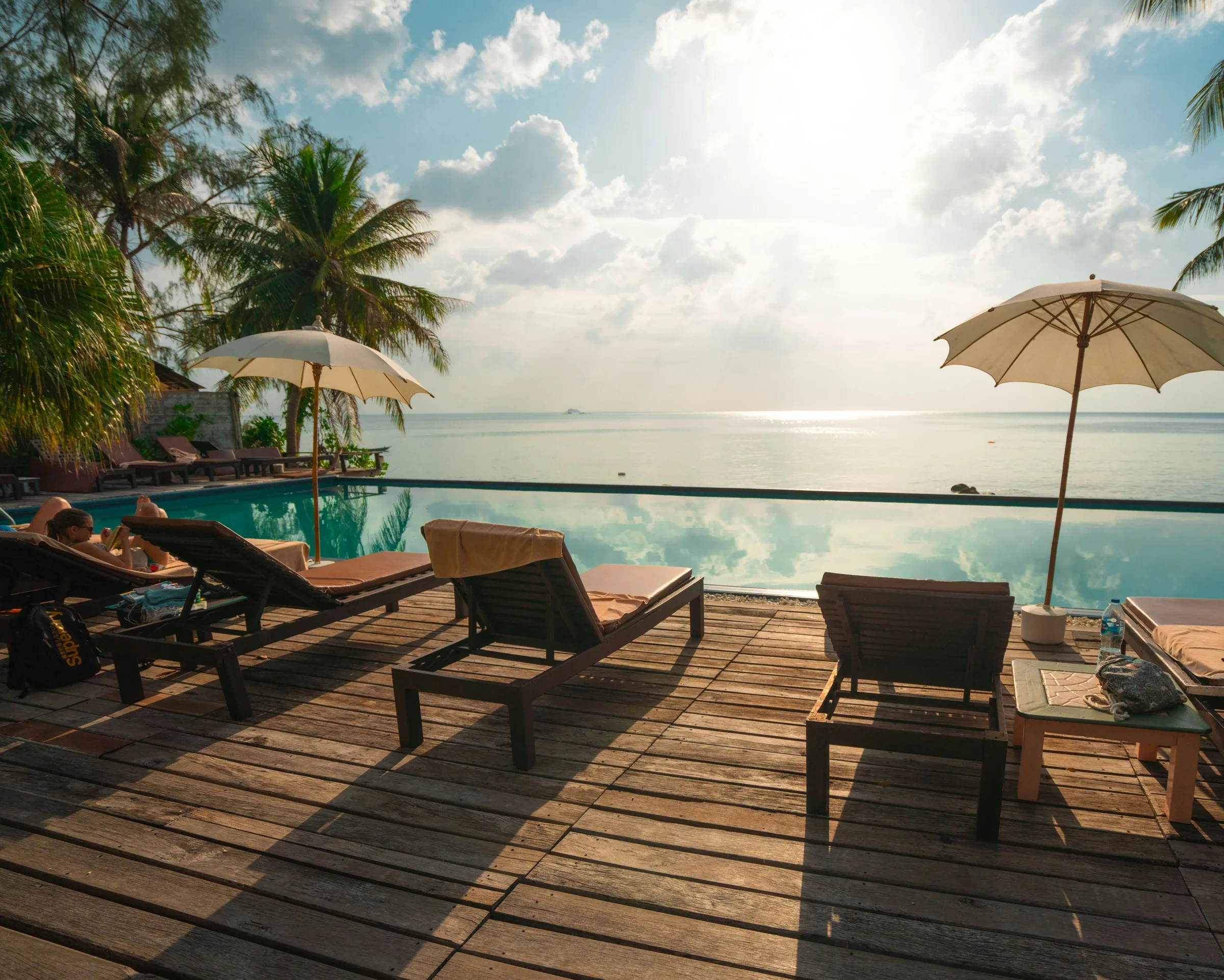 Sun loungers beside a sea-view infinity pool on a timber terrace