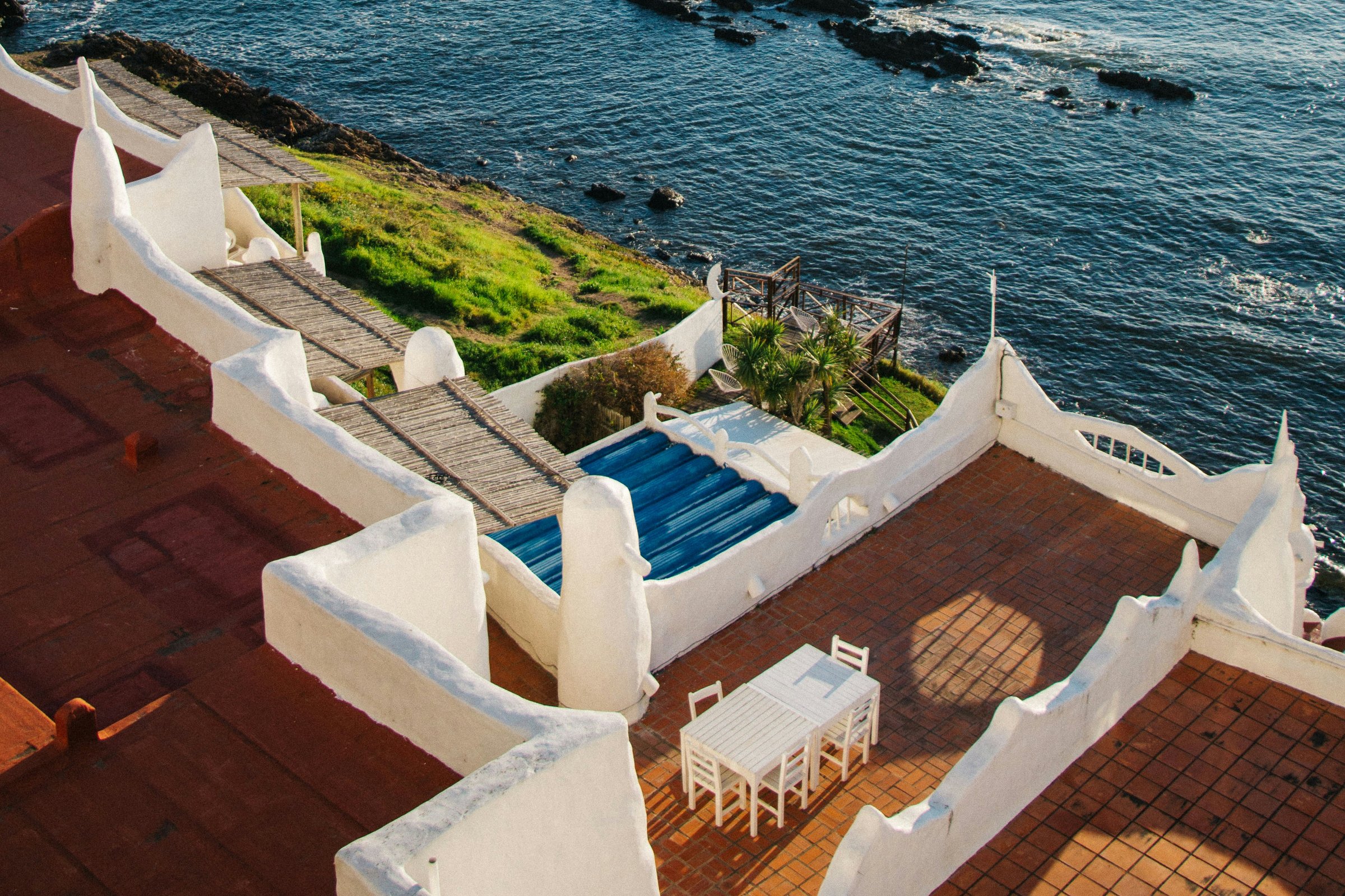 White seaside terraces with terracotta tiles, timber pergolas and an open view of the ocean